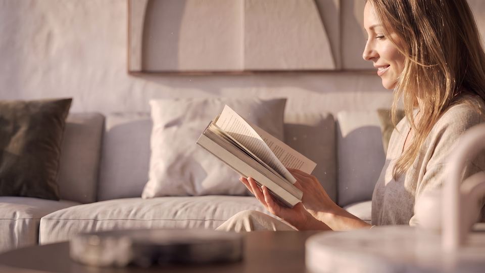 A woman reading a book on the living room sofa